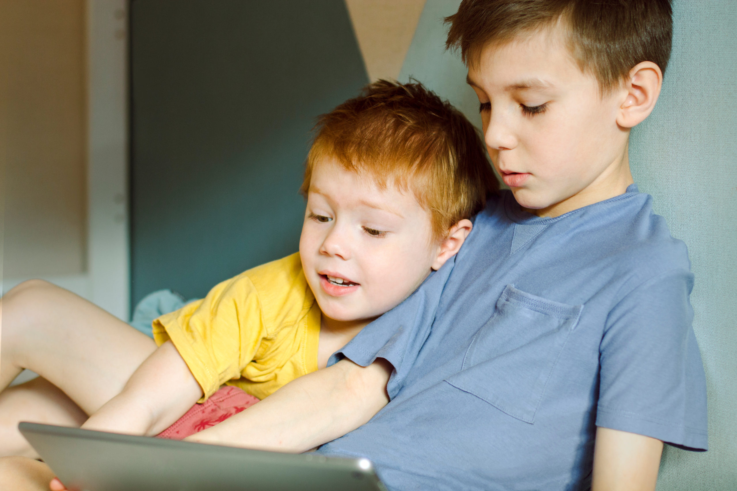 two boys aged 10 and 4 study something on a computer tablet toge